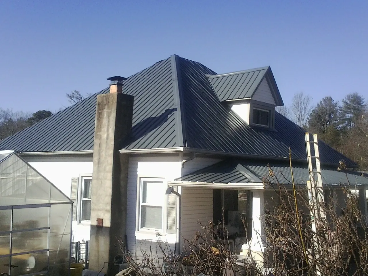 Dark blue standing seam metal roof on a white farmhouse with dormer — Slate & Tile Roof Repair by Roofing Brothers in Laconia
