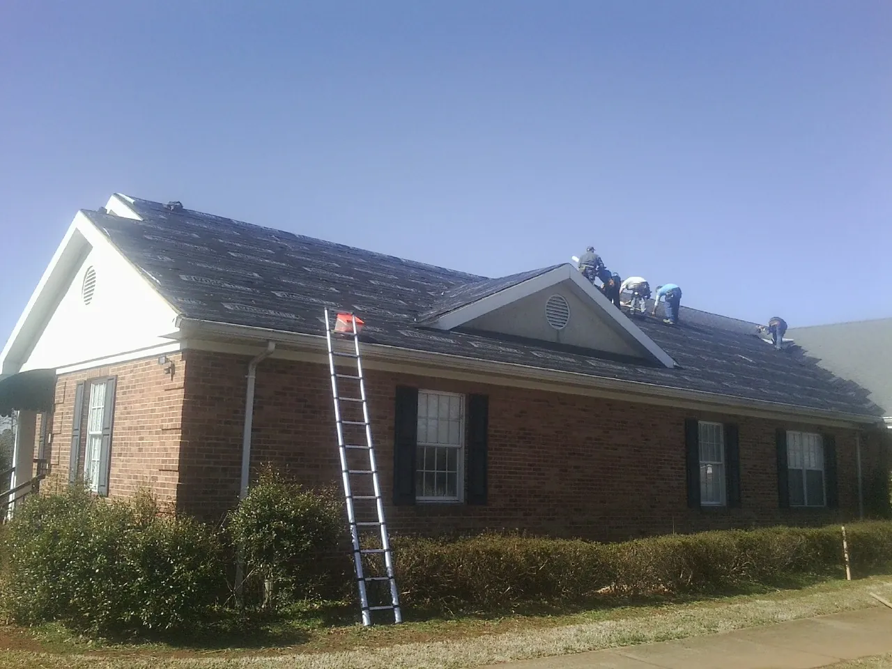 Crew tearing shingles off a brick ranch roof with a ladder set — Emergency Roof Repair work by our crew in Laconia
