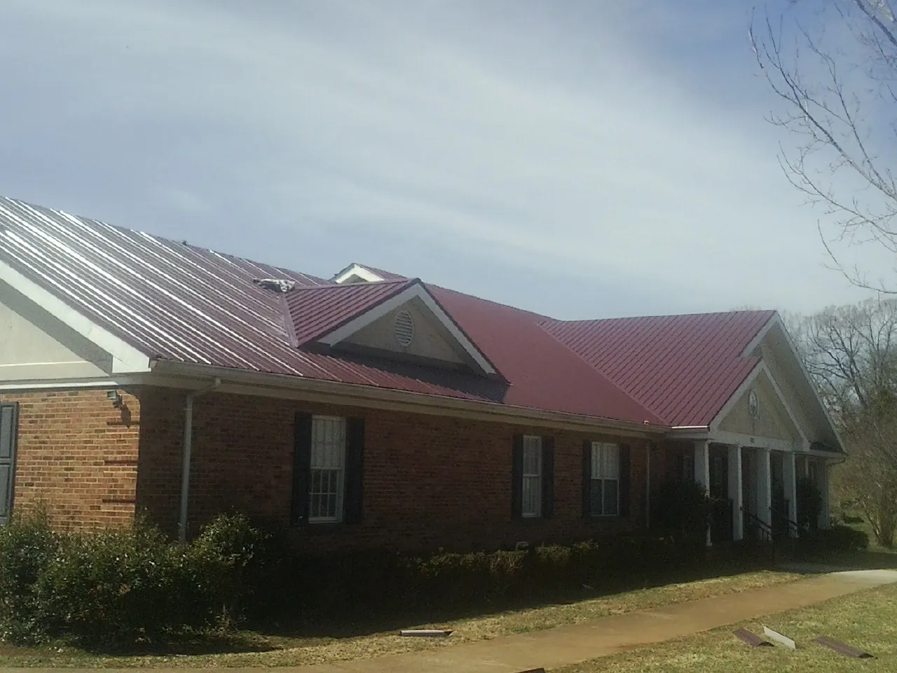 Red metal roof with gabled entries on a long brick building, from a Hail Damage Roof Repair job in Laconia