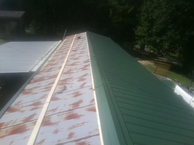 Old rusted panels beside newly installed green metal roofing — Wind Damage Roof Repair by Roofing Brothers in Laconia