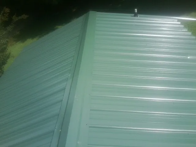 New green metal panels meeting at the ridge of a roof — Flat Roof Repair work by our crew in Laconia