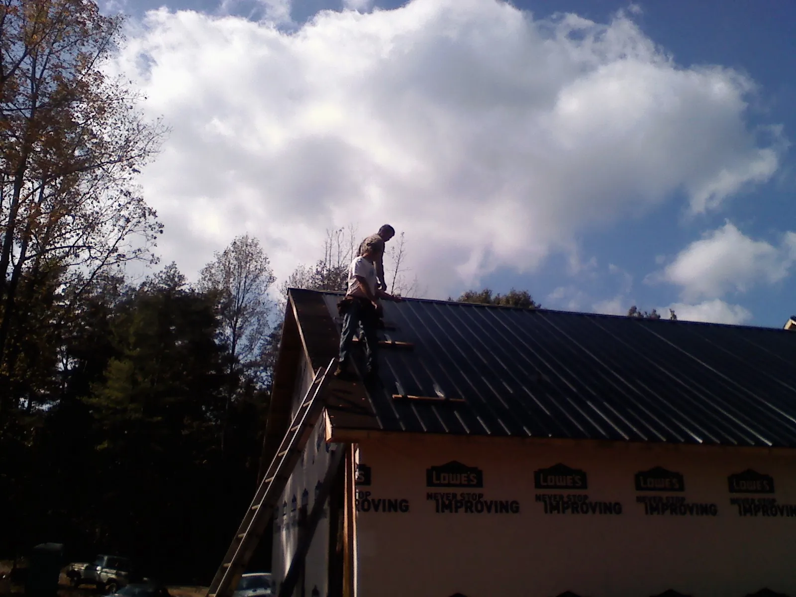 Roofer fastening dark metal panels high against a cloudy sky, from a Roof Inspection job in Laconia