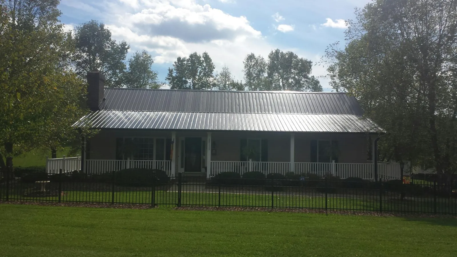 Gray metal roof on a brick ranch with a full width front porch — Gutter Guard Installation work by our crew in Laconia