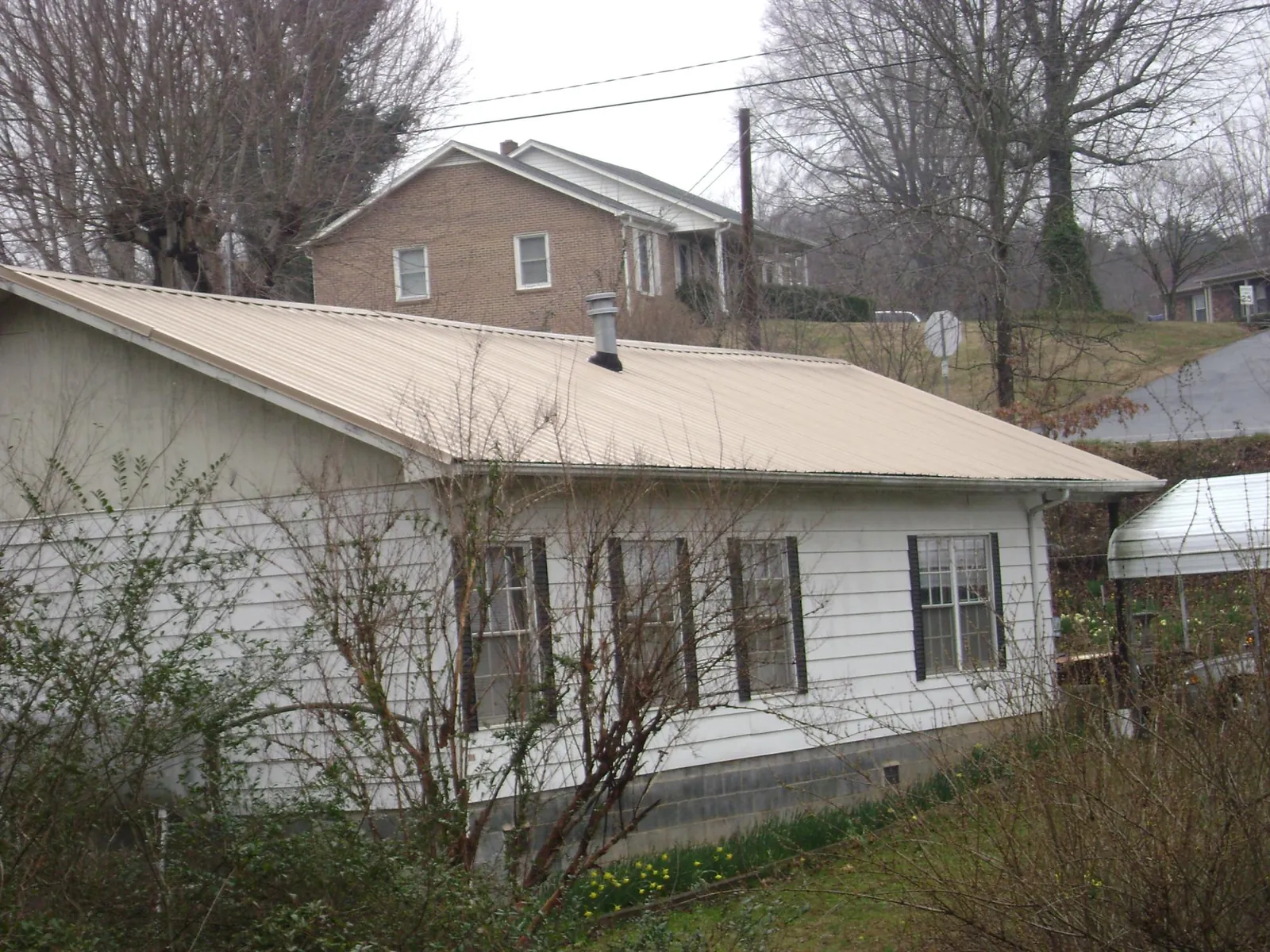 Tan metal roof on a white sided house set into a hillside — Commercial Roofing by Roofing Brothers in Laconia