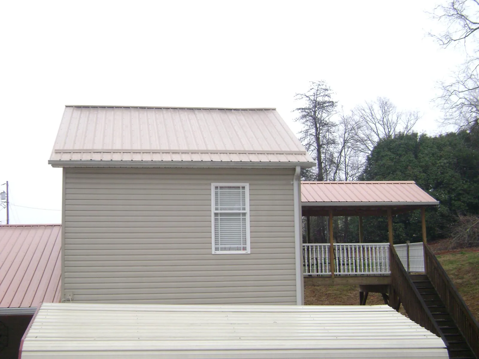 Tan metal roofs on a two story addition and attached porch, from a Roof Replacement job in Laconia